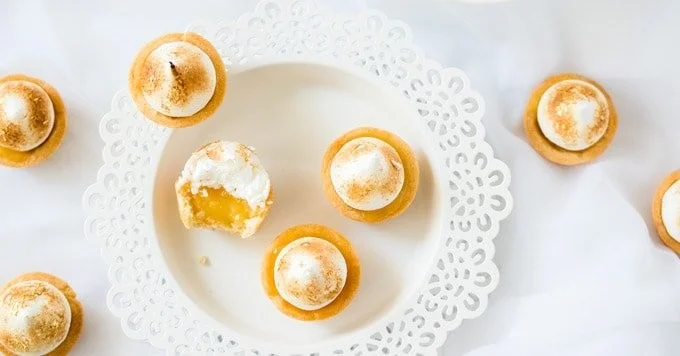 Zesty mini lemon meringue pies on a plate, topped with fluffy meringue
